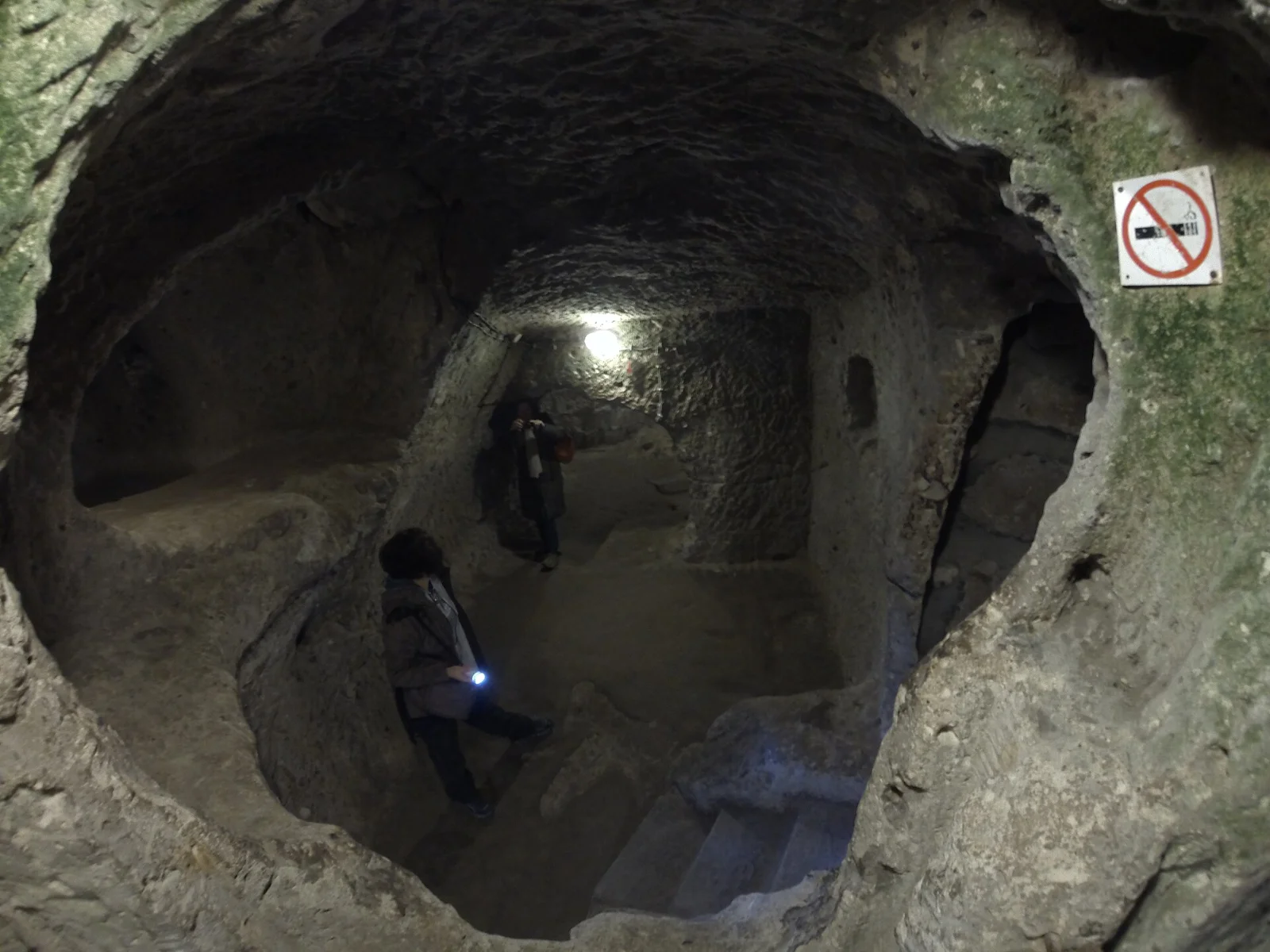 Visitors seen at a distance in a rock-cut Derinkuyu chamber with modern rails